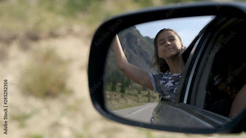 The girl relaxes in a moving car while sitting by the window against the backdrop of the mountains. Reflection in a car mirror. Journey. The girl relaxes in a moving car while sitting by the window against the backdrop of the mountains. Reflection in a car mirror. Journey.