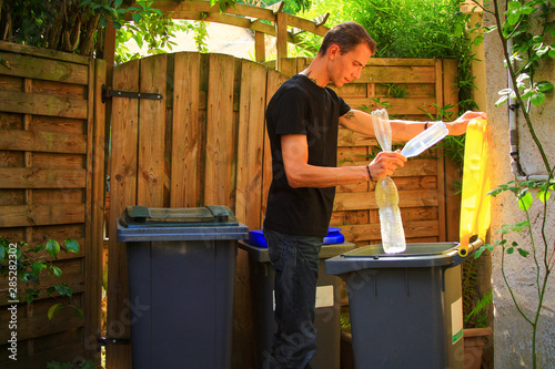Person making a selective sorting of waste. Man putting plastic bottles in a yellow bin for recycling.