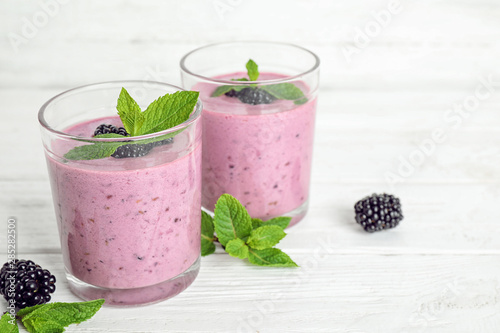 Delicious blackberry smoothie in glasses on white table, space for text