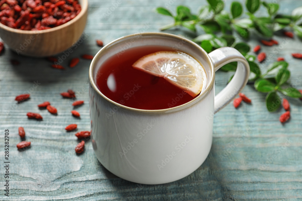 Healthy goji tea with lemon in cup on blue wooden table Healthy goji tea with lemon in cup on blue wooden table