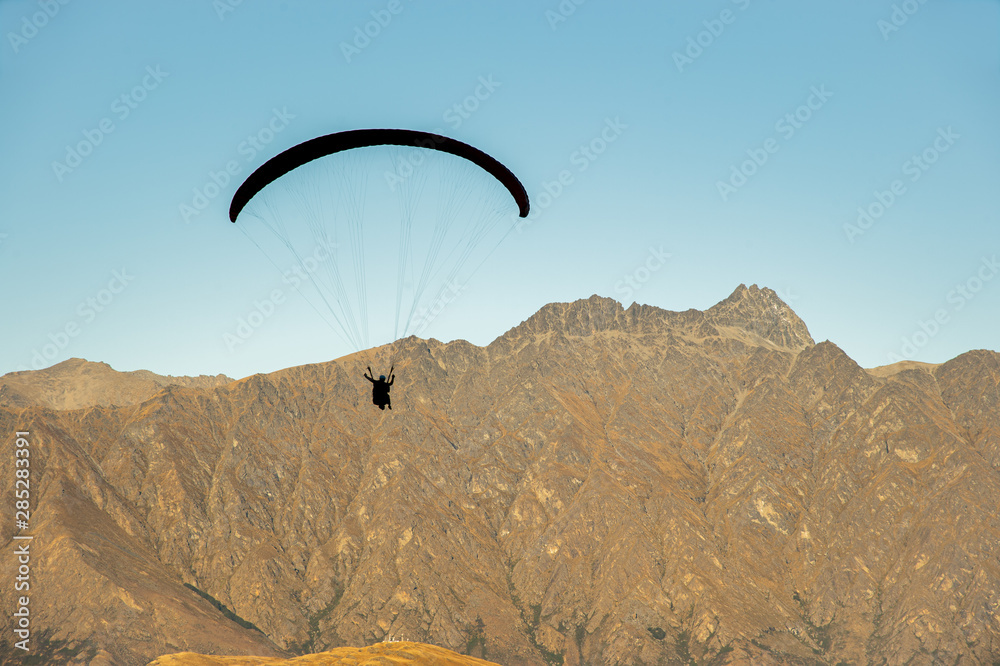 Paragliding on beautiful clear blue sky over mountain, most popular extreme sport in Queenstown, New Zealand. Paragliding on beautiful clear blue sky over mountain, most popular extreme sport in Queenstown, New Zealand.