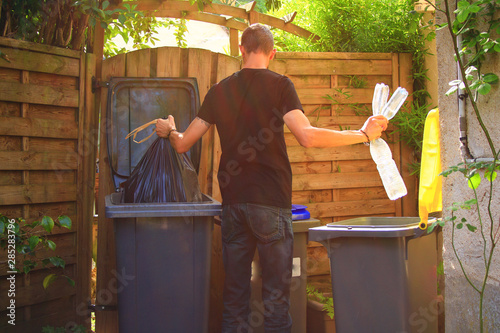 Person performing a selective sorting of household waste in recycling bins. Man putting plastic bottles in a yellow container and garbage in a bag in a green container. photo