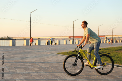 Handsome young man riding bicycle on city waterfront