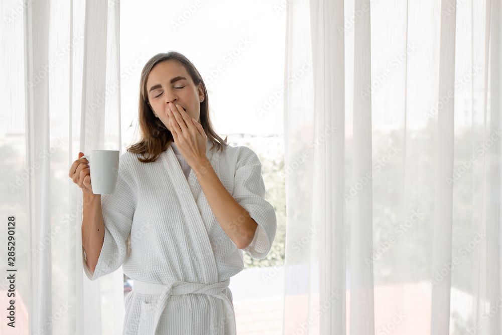 Caucasian woman in pajamas holding a glass of white coffee ready to drink by the window. Caucasian woman in pajamas holding a glass of white coffee ready to drink by the window.
