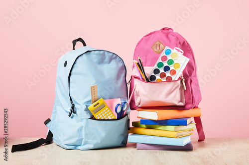 Foto blue and pink backpacks with school supplies near books isolated on pink