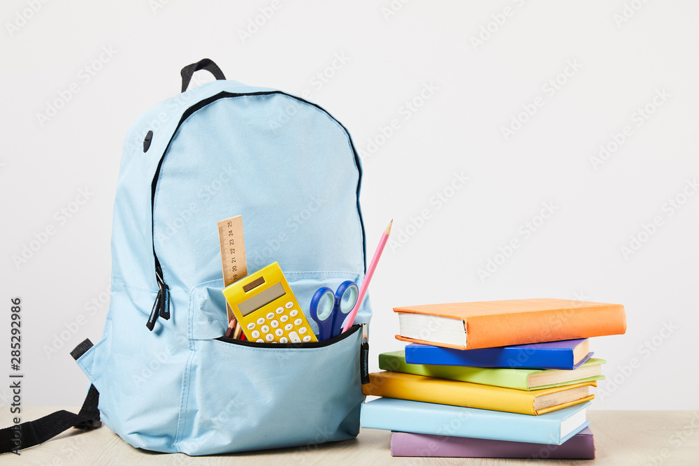 blue backpack with school supplies near books isolated on white - obrazy, fototapety, plakaty 