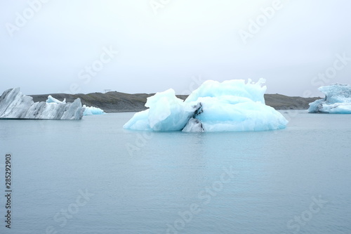 Overview of a very crystalline blue iceberg in Iceland on a calm sea and a white sky