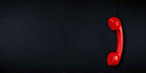 red  colored old fashioned retro phone reciever with black telephone wire dark slate blackboard background with copy space. business communication support service problem and solution concept