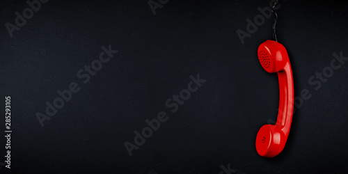 red  colored old fashioned retro phone reciever with black telephone wire dark slate blackboard background with copy space. business communication support service problem and solution concept photo