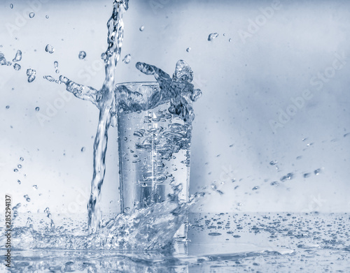 Water splashes and pouring water into glass on blue background