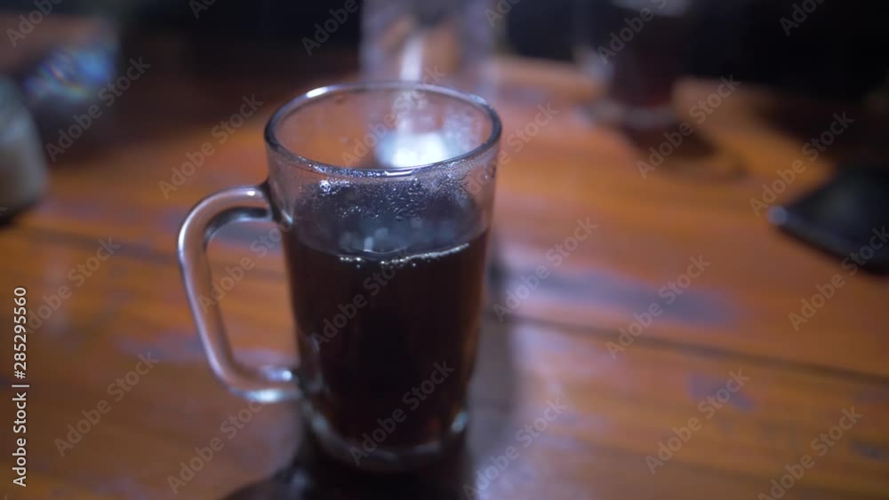 Steaming hot cup of coffee in a tall clear glass mug resting on a wooden table. Close up view with camera orbiting. Steaming hot cup of coffee in a tall clear glass mug resting on a wooden table. Close up view with camera orbiting.
