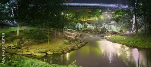 Liberty bridge night view from Greenville Falls park in South Carolina with foreground river with lights reflections and downtown oasis park and waterfalls lighten by it photo