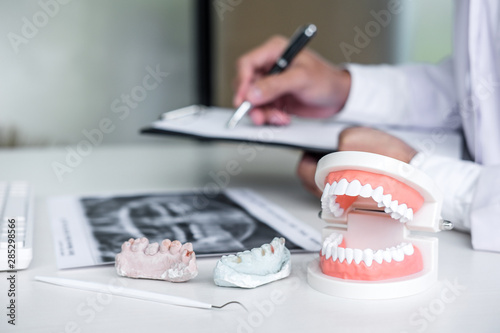 Foto Male doctor or dentist writing report working with tooth x-ray film, model and e