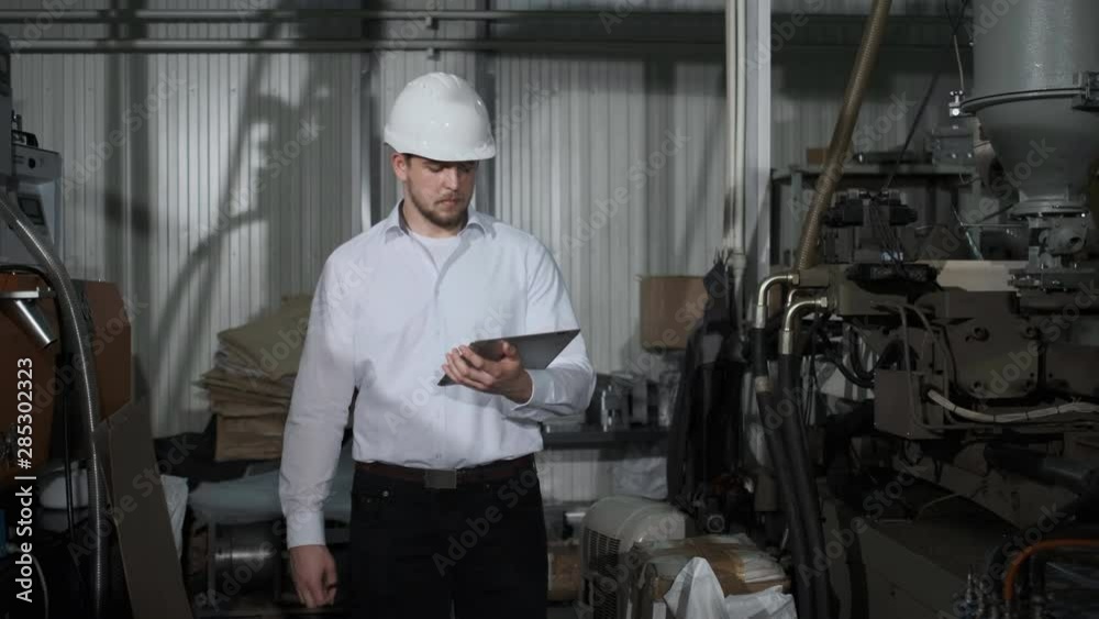 Shot of Professional Factory Worker Wearing Hard Hat Holds Tablet Computer, Walking Thorugh Modern Industrial Manufacturing Facility. 4k Shot of Professional Factory Worker Wearing Hard Hat Holds Tablet Computer, Walking Thorugh Modern Industrial Manufacturing Facility. 4k