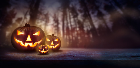 Spooky Jack O' Lanterns at sunset, dusk in pine forest towering up in the background at night.