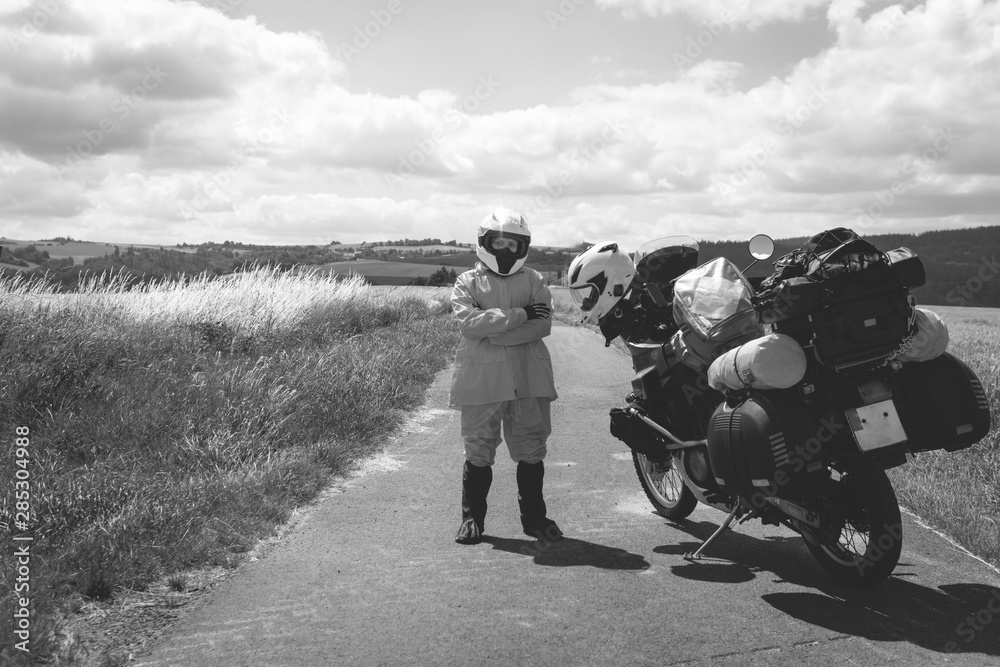 The driver girl in helmet is wearing a raincoat. Adventure motorbike with side bags. a motorcycle tour journey. Outdoor. black and white, bw, freedom concept. field and sky on background, copy space