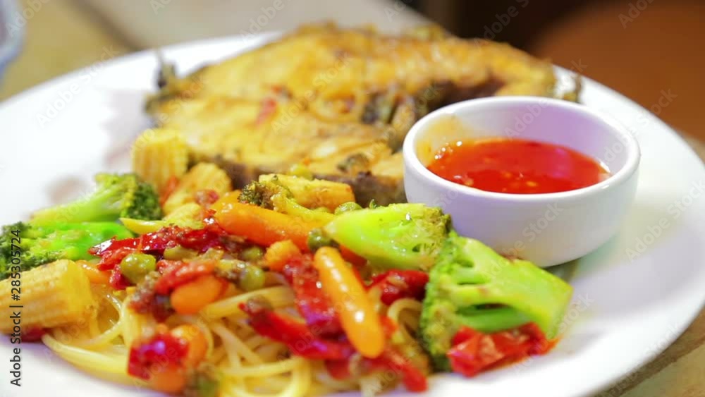 A white plate of fish and spaghetti with vegetables and sauce rotates in a circle A white plate of fish and spaghetti with vegetables and sauce rotates in a circle