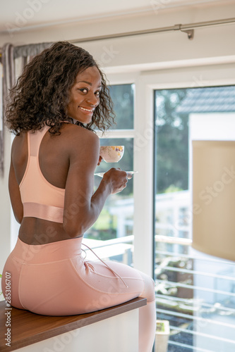 Beautiful young fit black female sitting in the kitchen drinking tea