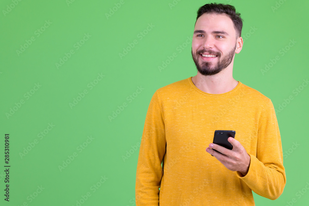 Happy young handsome bearded man thinking while using phone Happy young handsome bearded man thinking while using phone
