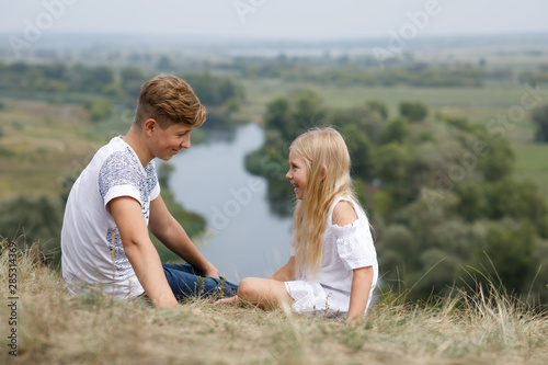 Boy and girl sits on the hill above the river