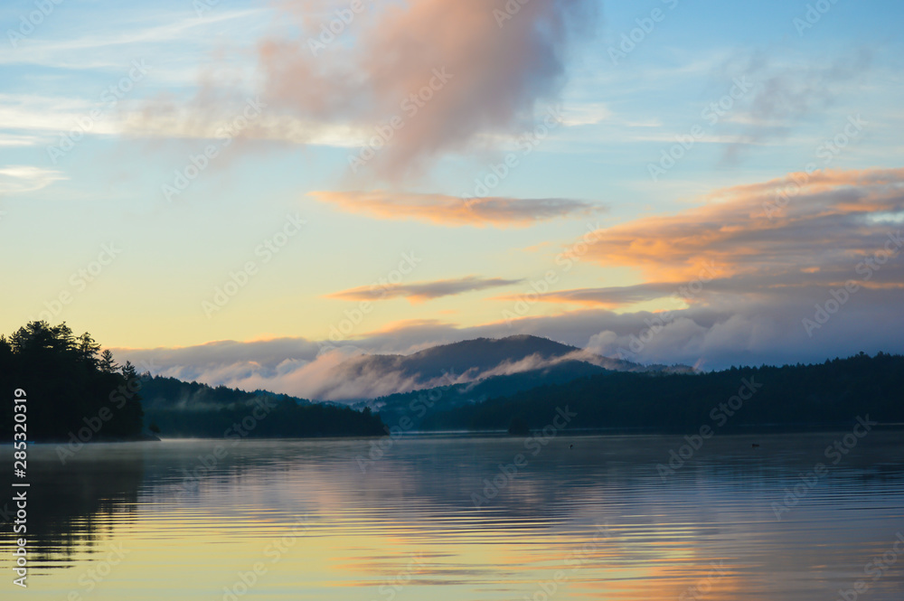 Sun rising over Saranac Lake with the mountains and rolling fog reflecting in the lake; two loons float on the water