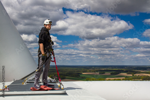young male worker standing on top of a wind turbine with cloudy sky in the background