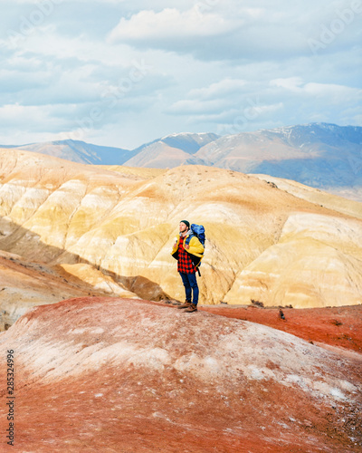 the guy traveler with the big backpack got on red mountains and admires a view photo