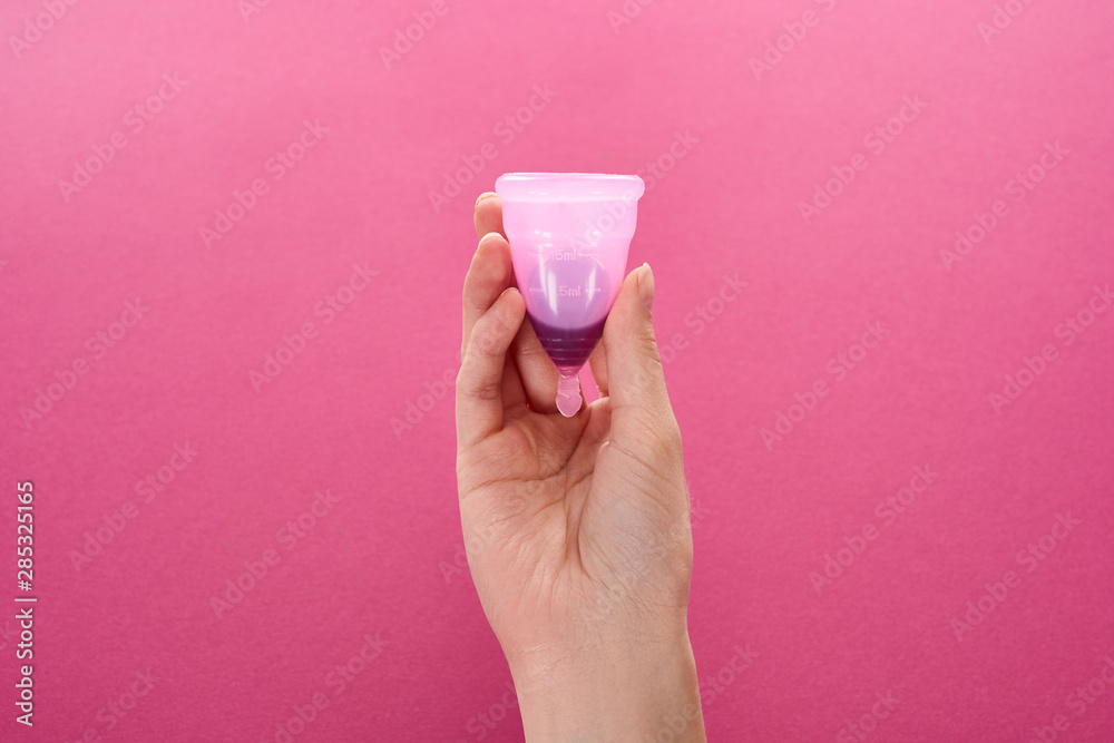 partial view of woman holding menstrual cup with blood on purple background partial view of woman holding menstrual cup with blood on purple background