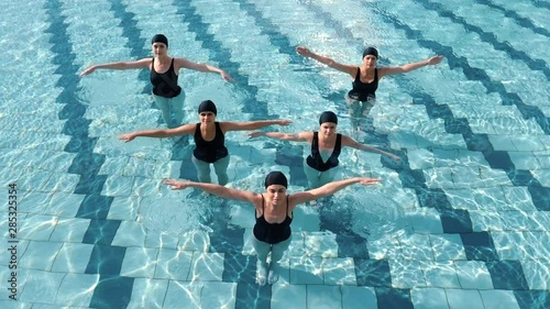 Five young girls do water aerobics in an open-air pool.  In the summer in the pool. 