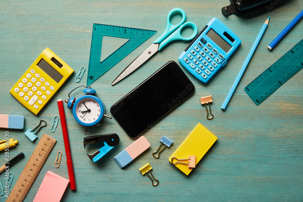 Top view of smartphone with blank screen near school supplies at turquoise wooden table Top view of smartphone with blank screen near school supplies at turquoise wooden table