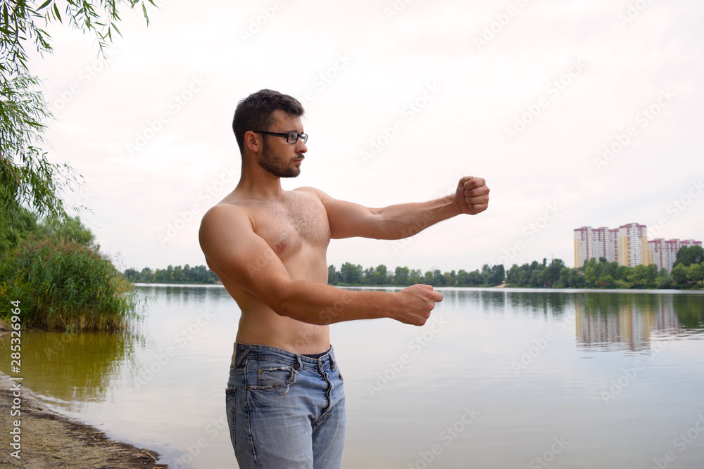 A young athletic muscular man stands near a lake in the city.