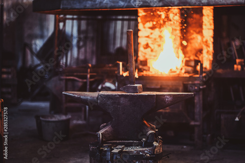 Vászonkép Hammer on anvil at dark blacksmith workshop with fire in stove at background