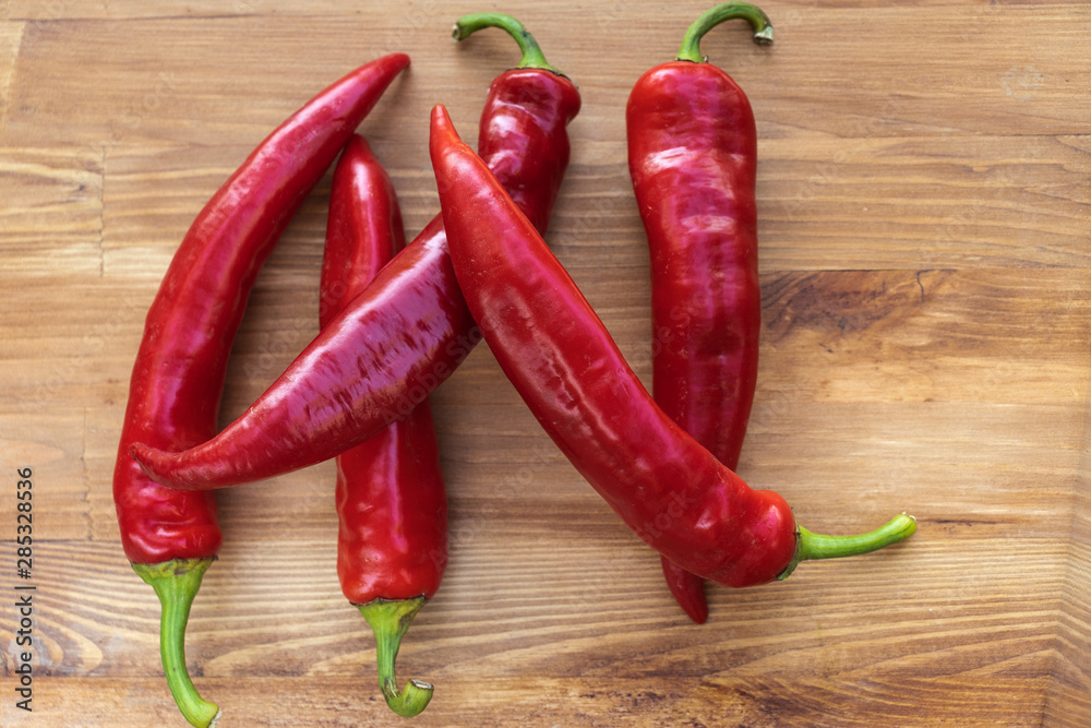 Five red hot chili peppers on a brown wooden background, top view