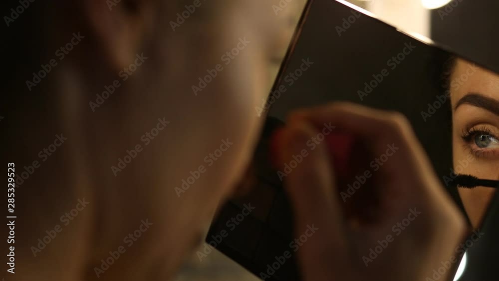 Woman applying mascara and looking to the mirror Woman applying mascara and looking to the mirror