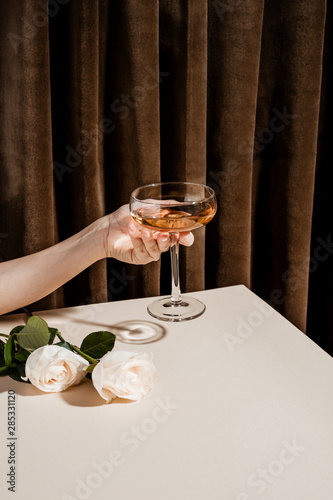 Close up view of hand holding champagne glass with white roses beside
