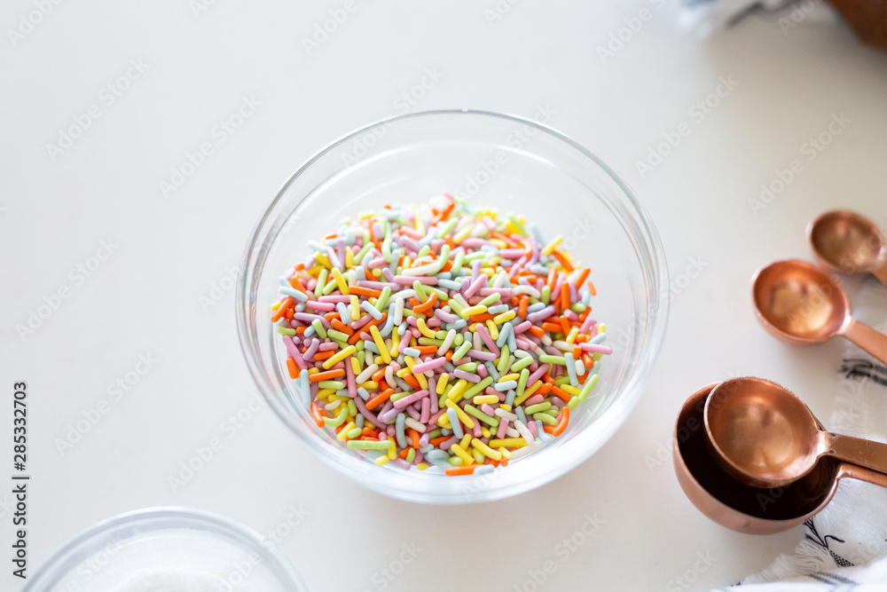 cake ingredients on white background, rainbow sprinkles in bowl cake ingredients on white background, rainbow sprinkles in bowl