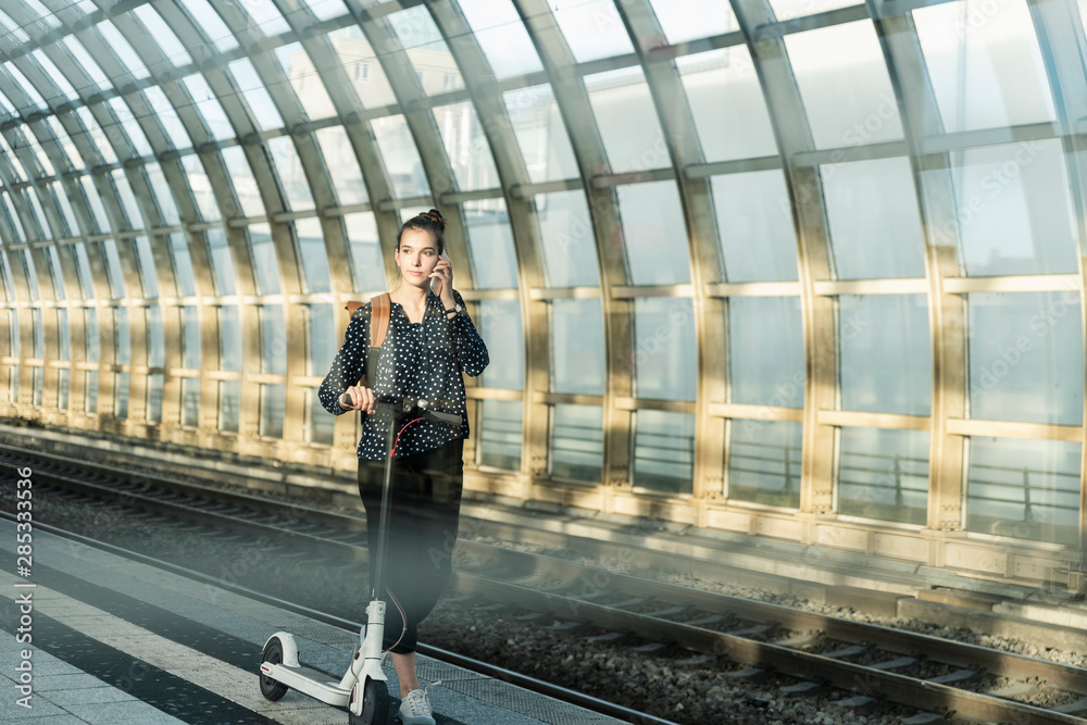 Young woman with electric scooter on cell phone at the train station Young woman with electric scooter on cell phone at the train station
