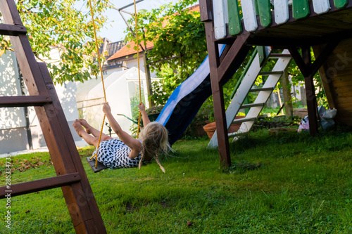 3-5 year old blond girl having fun on a swing outdoor. Summer playground. Girl swinging high. Young child on swing in garden