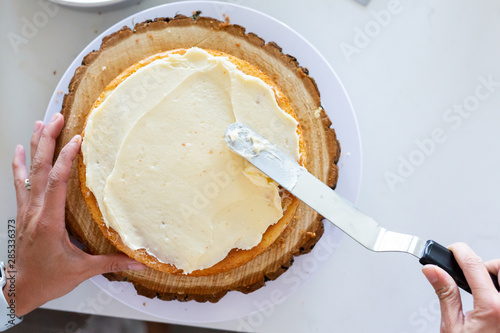 woman icing vanilla cake with metal spatula 
