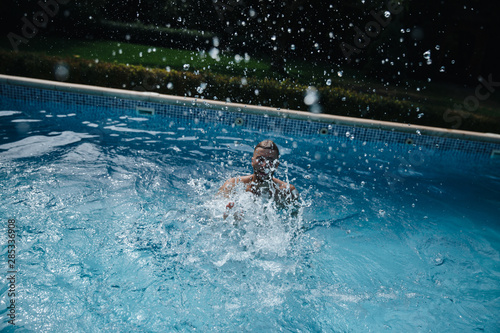 Young man swimming in the swimming pool splashing water. Up viiew
