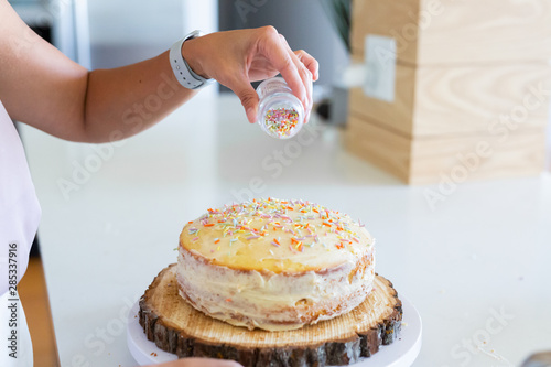 Woman pouring sprinkles onto cake