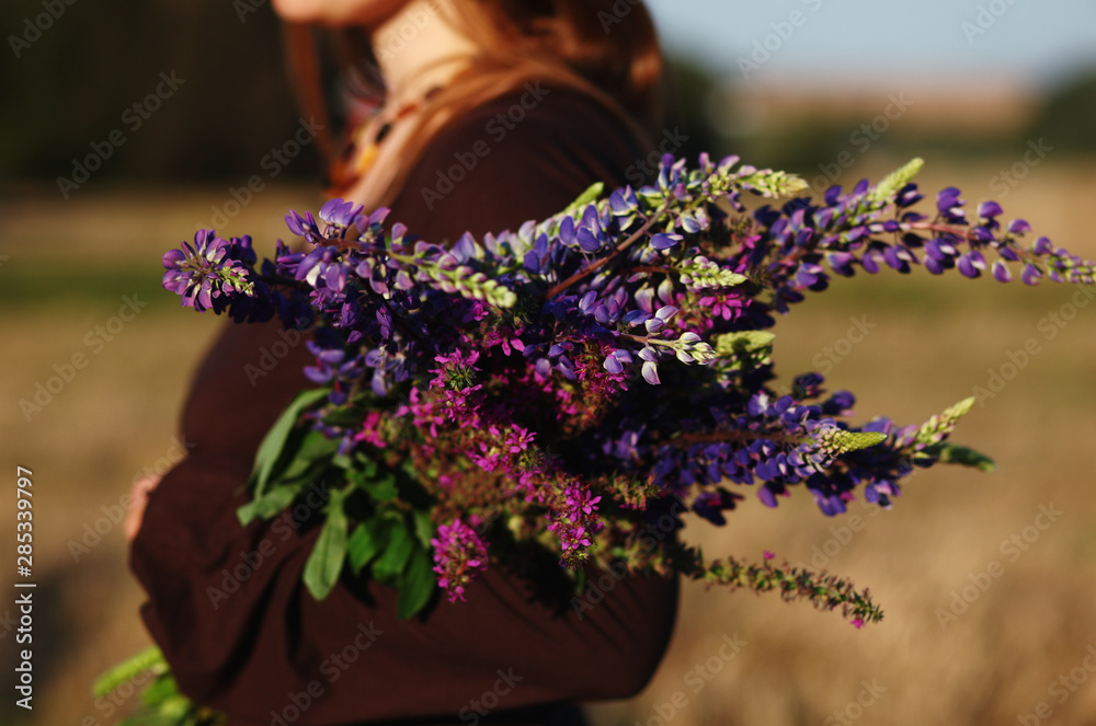 woman holding a bouquet of wildflowers lupines against rural landscape woman holding a bouquet of wildflowers lupines against rural landscape