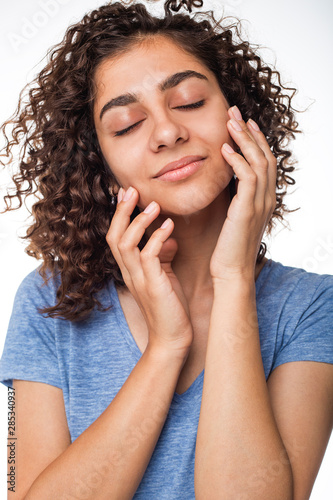 Portrait of a beautiful young mixed race brunette woman with natural makeup, touching her clean skin on her face on a white isolated background. 