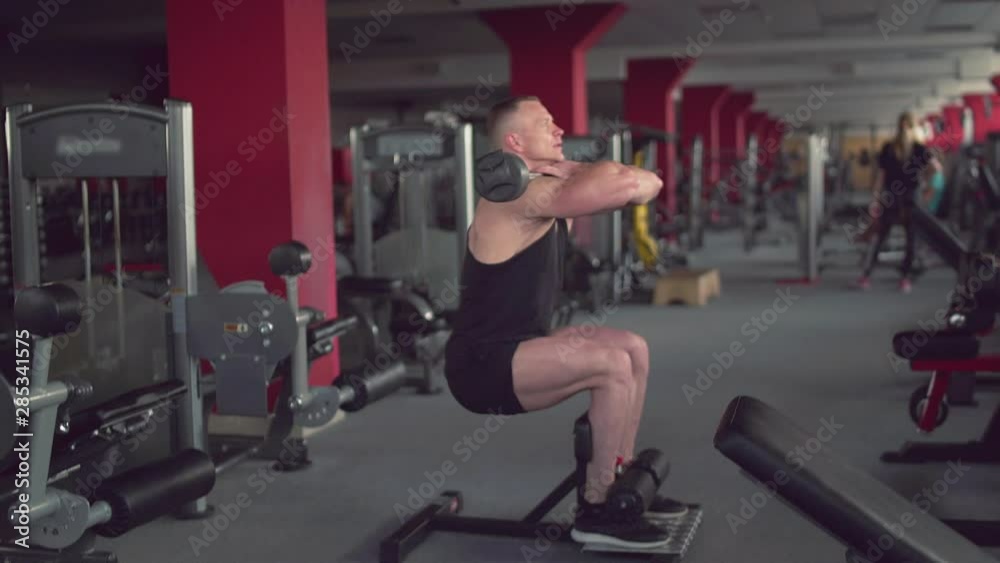 Professional muscular athlete makes squats with a bar at the gym Professional muscular athlete makes squats with a bar at the gym