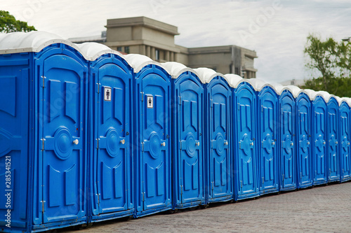 Long row of portable bio toilet cabins in a city street. Line of chemical toilets for the holiday, festival and crowd of people. Blue cabines of bio toilets in the city center. WC.