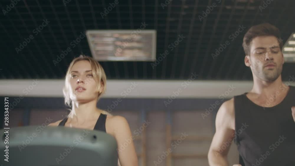 Concentrated couple running together on treadmill machine in gym club. Concentrated couple running together on treadmill machine in gym club.