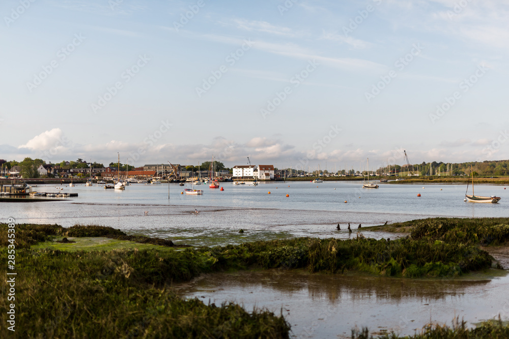 A view of the Tide Mill with the river Deben in the foreground. There are row boats and small fishing boats moored up in the river
