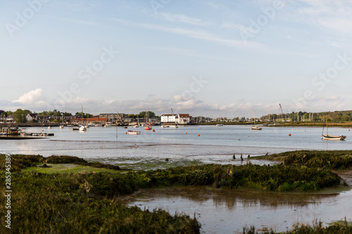 A view of the Tide Mill with the river Deben in the foreground. There are row boats and small fishing boats moored up in the river