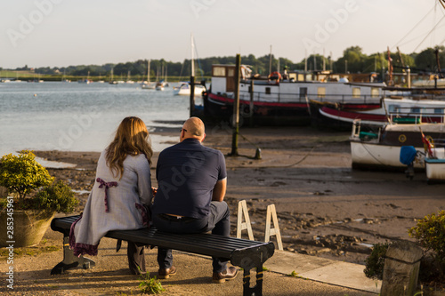 A married couple sitting in the golden evening sun watching the sunset over a river © Collins Photography