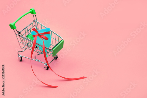 blue menstrual cup with a red bow as a bonus or gift in a mini Supermarket Trolley on a pink isolated background